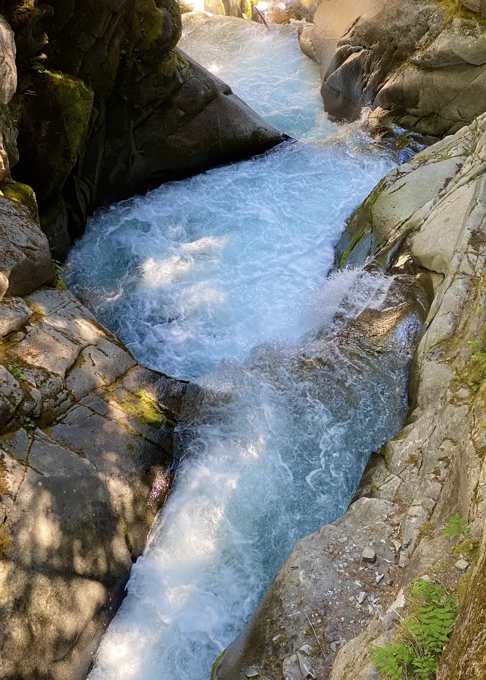 Turquoise whitewater rushes through a narrow channel between large moss-covered rocks.