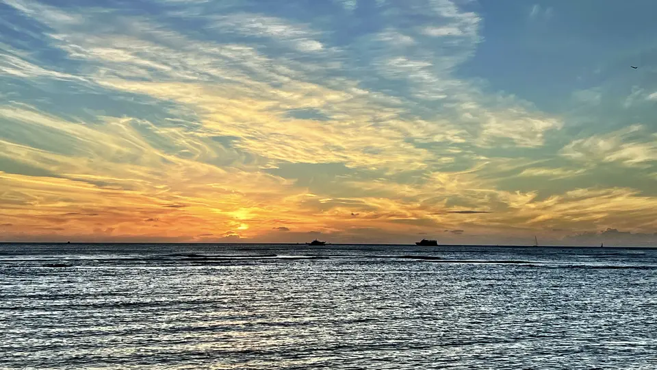 The sun sets over rippling ocean water beneath a sky streaked with glowing clouds.