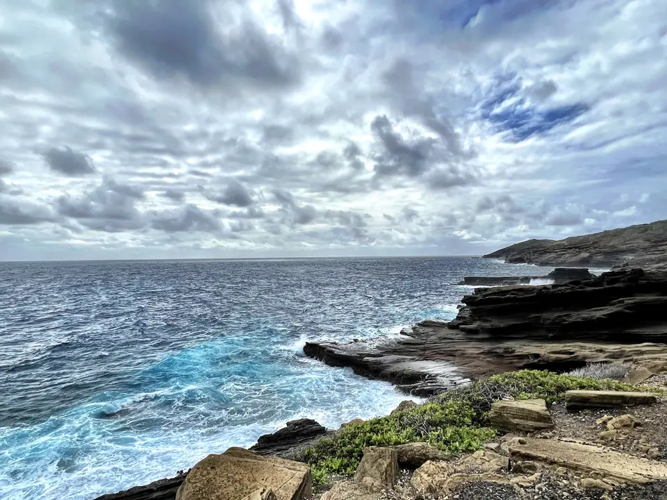 Waves wash against a layered rocky shoreline beneath a dramatic cloud-filled sky.
