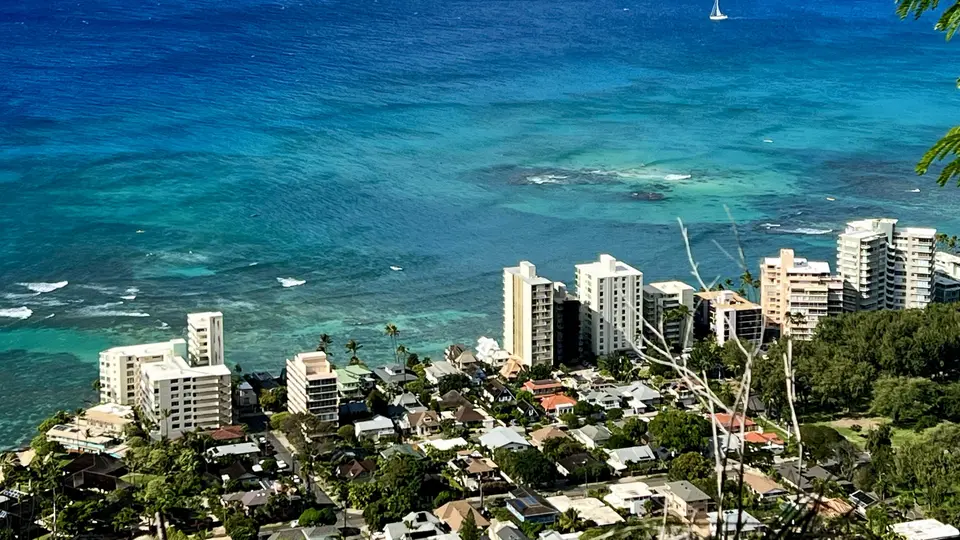 Turquoise ocean water stretches beyond a dense cluster of coastal high-rise buildings and houses.