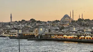 Galata Bridge spans choppy water below a dense hillside of buildings and a domed mosque at sunset.