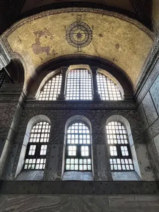 Tall arched windows rise beneath a gilded vaulted ceiling with a circular ornamental mosaic, above veined marble walls.