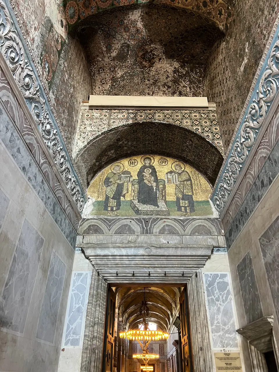 The Hagia Sophia’s mosaic of the Virgin and Child is framed by a marble arch above an ornate vaulted corridor with glowing chandeliers.