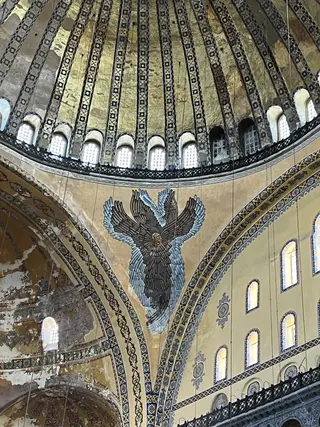 The interior of Hagia Sophia shows a gilded dome, patterned arches, and a large winged mosaic above rows of arched windows.