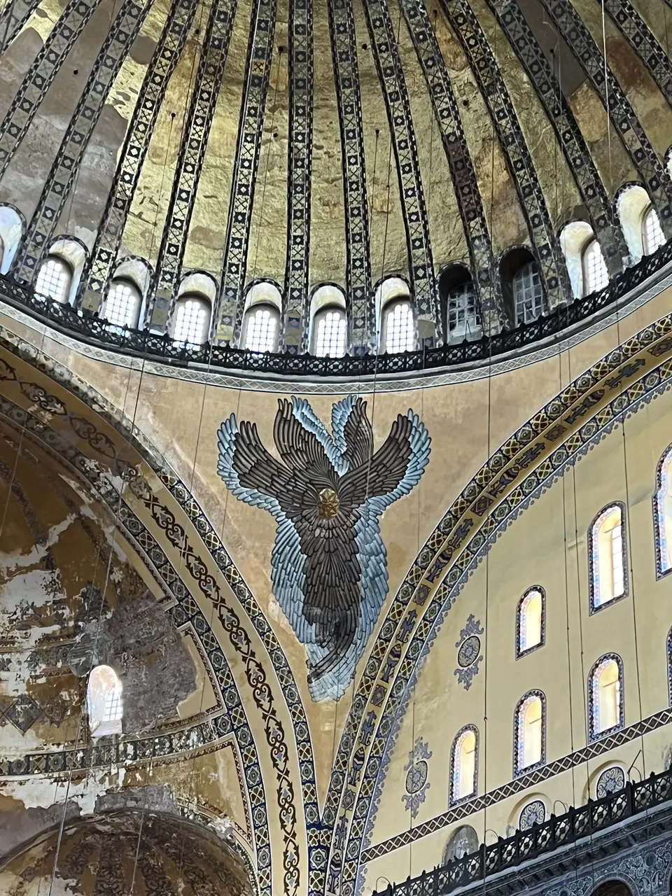 The interior of Hagia Sophia shows a gilded dome, patterned arches, and a large winged mosaic above rows of arched windows.