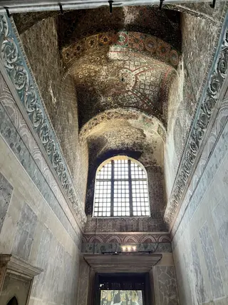 An arched marble interior passage rises to a patterned vaulted ceiling above a large gridded window.