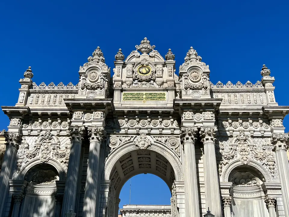 The elaborately carved stone entrance gate of Dolmabahçe Palace stands against a clear blue sky.