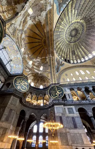 The soaring interior of Hagia Sophia features weathered painted domes, Arabic calligraphic medallions, marble arches, and glowing chandeliers.