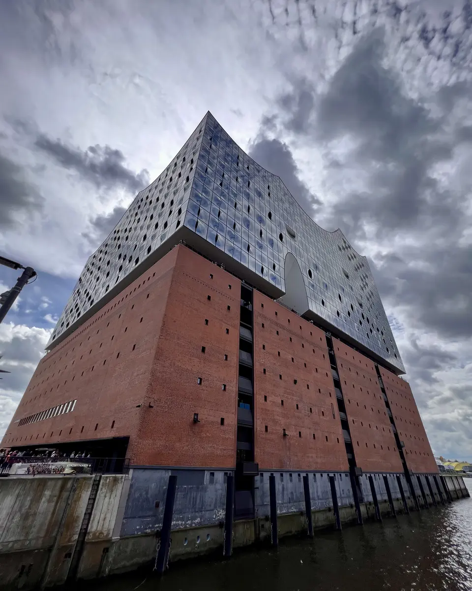 A large brick-and-glass waterfront building rises beneath dramatic gray clouds.