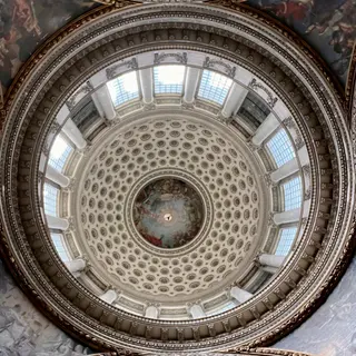 An ornate circular domed ceiling features painted murals, decorative coffering, white columns, and a ring of skylights.