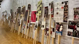 A row of wooden display stands holds illustrated posters and text panels along a patterned gallery wall.