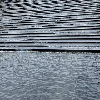 Thin sheets of water cascade down broad, dark stone steps into a rippling tiled pool.