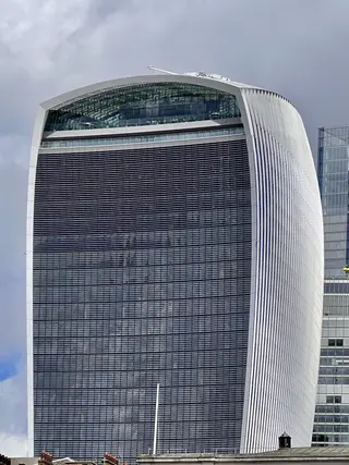 A tall modern office tower with a curved white frame and a dark louvered glass facade rises against a cloudy sky.