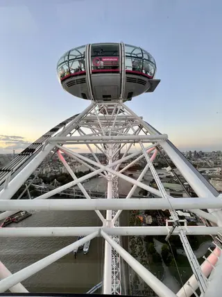A glass observation capsule bearing a lastminute.com London Eye sign rises above the white framework of a giant wheel, with a river and city skyline below.