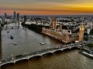 The Palace of Westminster and Elizabeth Tower stand beside the River Thames as Westminster Bridge carries traffic beneath a glowing sunset sky.