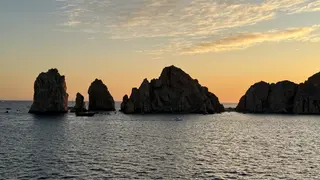 Jagged rocky sea stacks rise from the ocean beneath a glowing sunset sky.