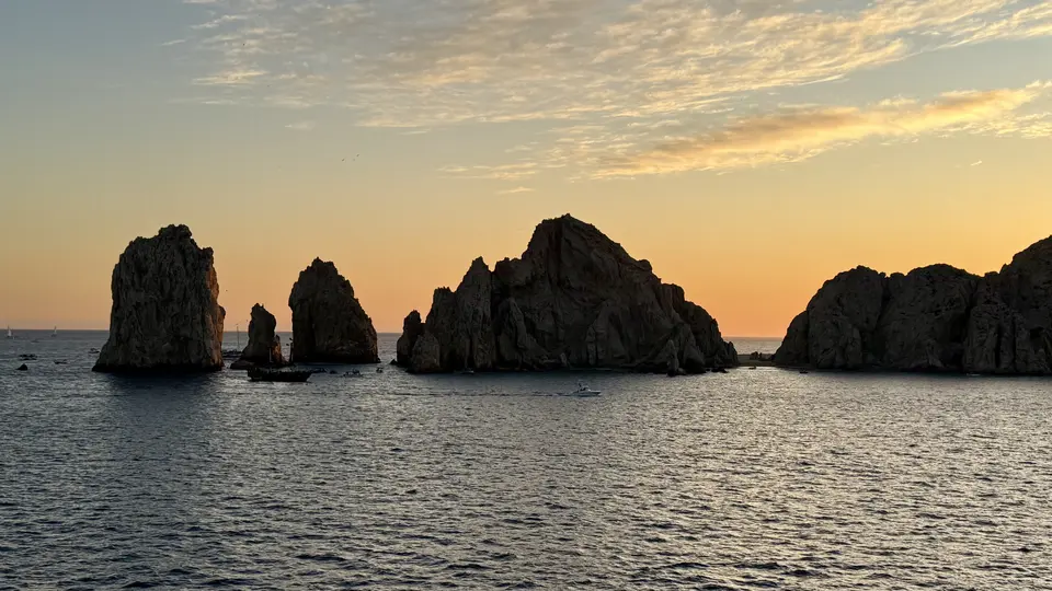 Jagged rocky sea stacks rise from the ocean beneath a glowing sunset sky.