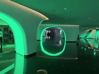 A futuristic interior corridor features glowing green circular archways reflected on a dark polished floor.