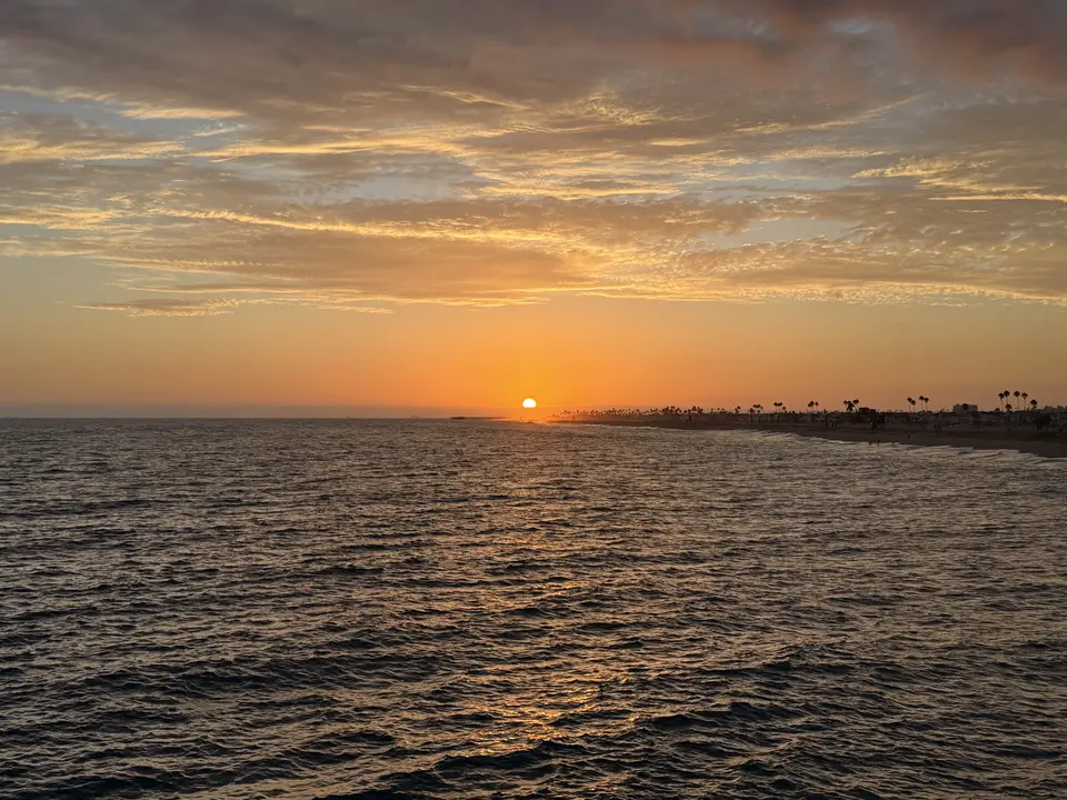 A golden sun sets over a beach with palm trees and waves.