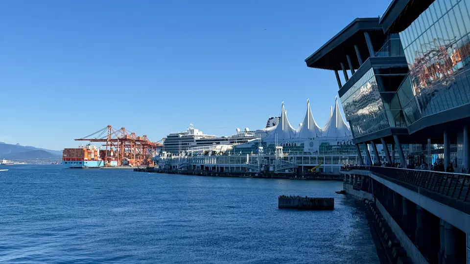 Canada Place and a cruise ship line the waterfront beside container cranes and modern glass buildings under a clear blue sky.