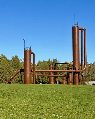 Rust-colored industrial towers and pipes from Gas Works Park rise above a grassy lawn beneath a clear blue sky.