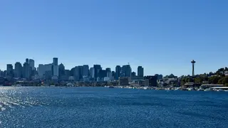 Seattle’s skyline and the Space Needle rise beyond sparkling water under a clear blue sky.